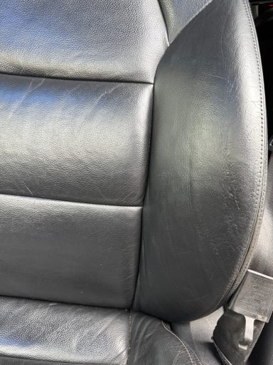 Détail d'un siège auto en cuir noir avec des coutures visibles.