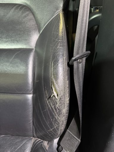 Détail d'un siège de voiture en cuir noir avec une usure visible.